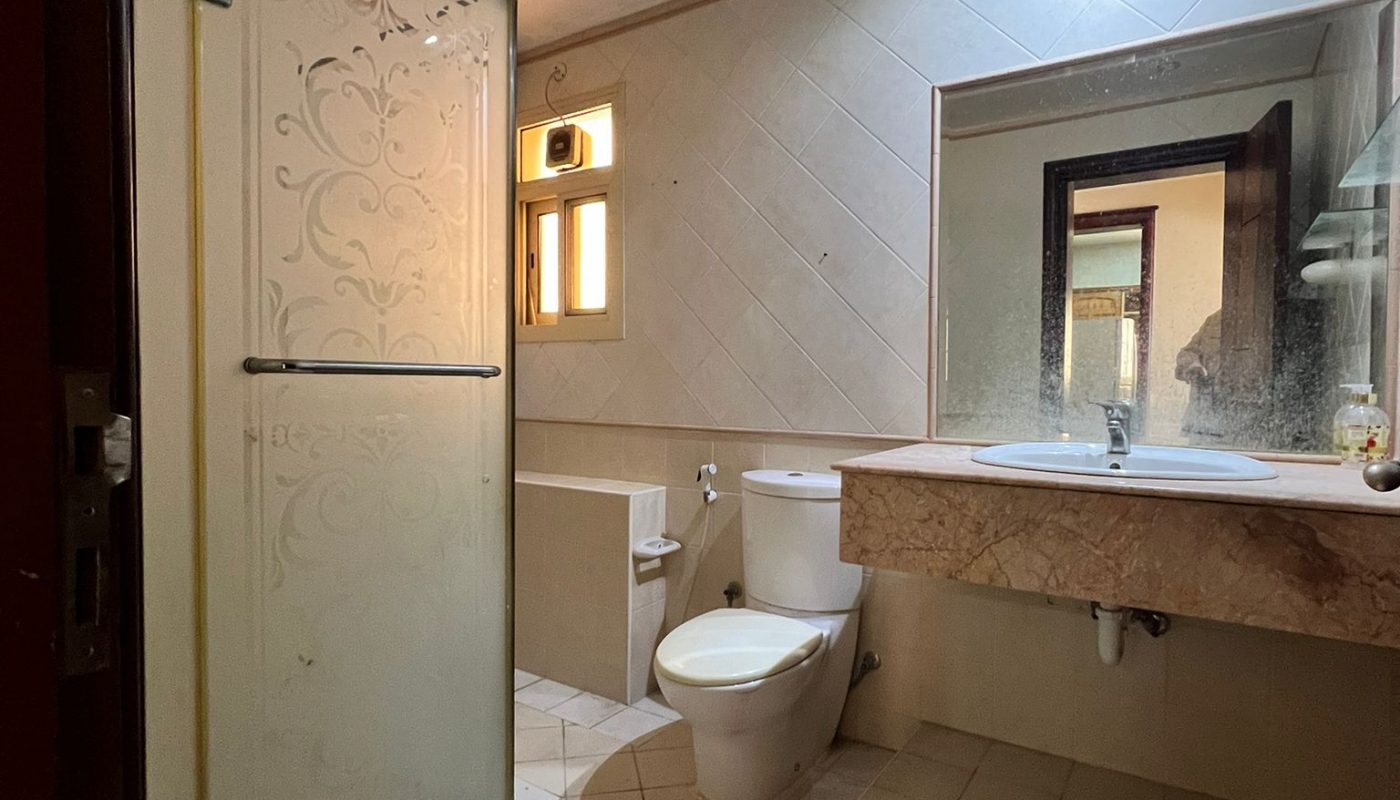 A bathroom with a toilet, sink, and shower stall. The floor is tiled, and there is a small window above the toilet.
