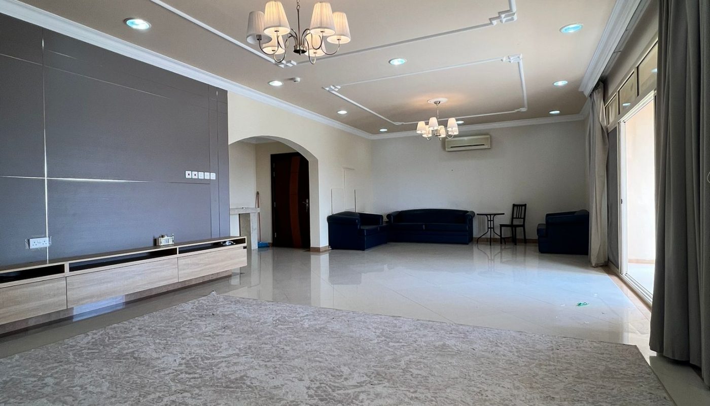 Spacious living room with light-colored tile flooring, a large rug, two sofas, wall-mounted shelves, chandeliers, and sliding glass doors with curtains.