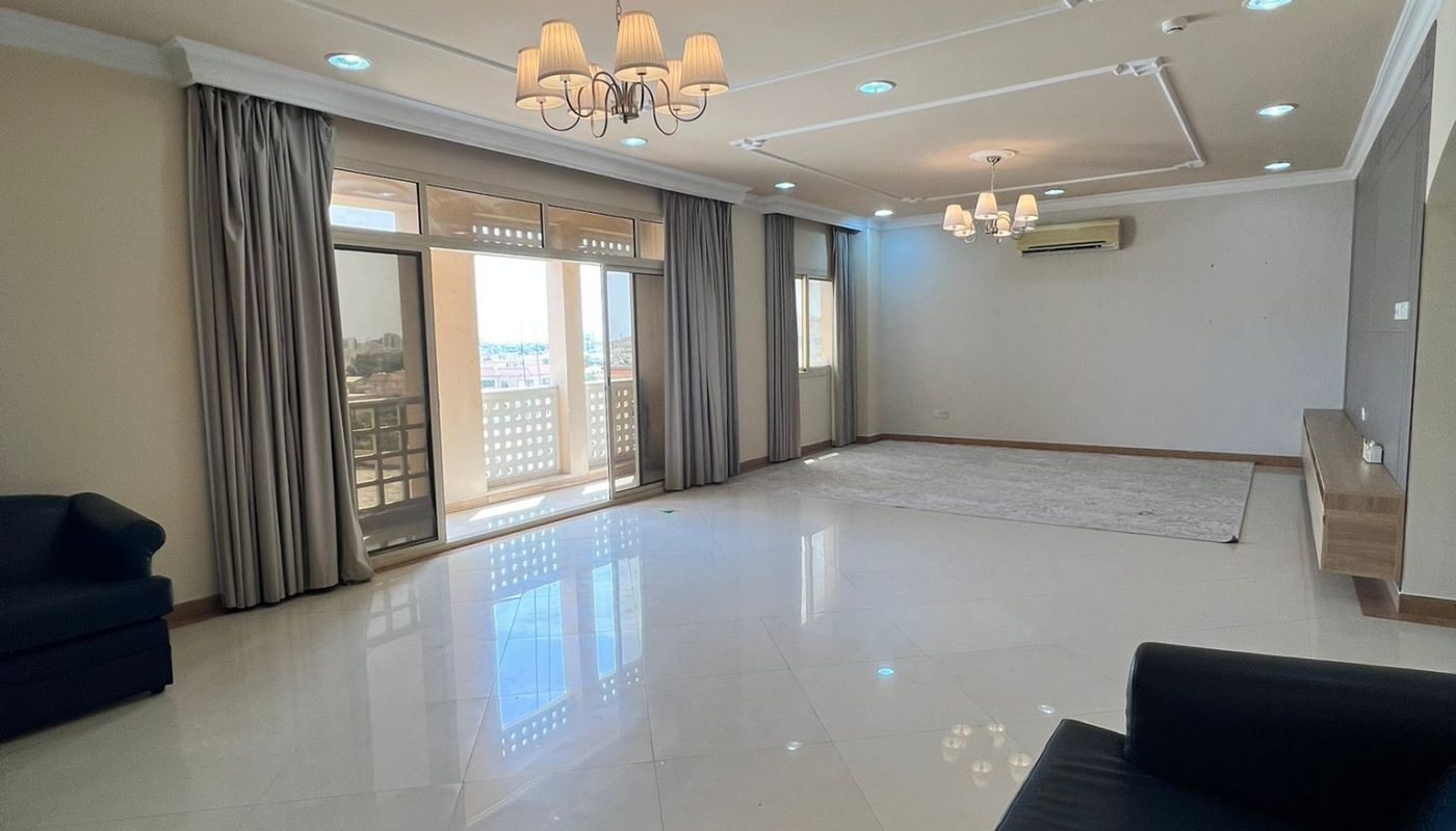 Spacious, unfurnished living room with tiled floor, black sofas, chandeliers, large windows with curtains, and a split air conditioning unit on the wall.