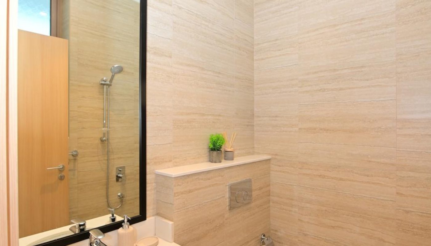 Modern bathroom with beige tiled walls, a wall-mounted toilet, a rectangular sink with a large mirror, and minimal decor including a small plant and toiletries.