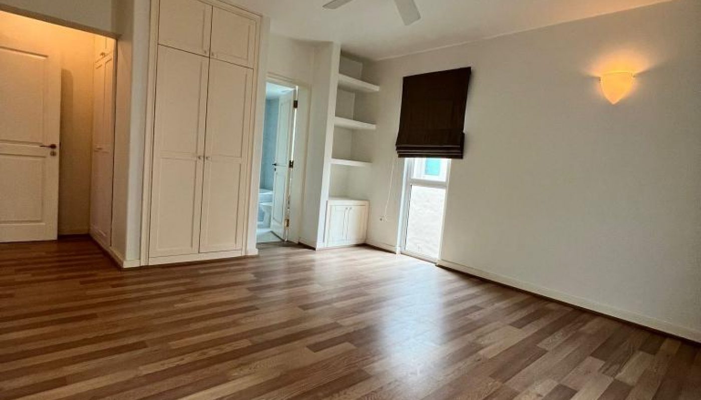 Unfurnished room with wooden flooring, white walls, ceiling fan, built-in shelves, closet, and a window with a brown shade; door leads to a bathroom.