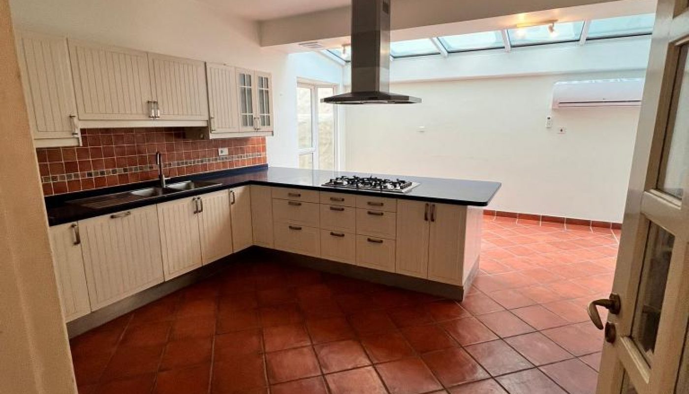 Kitchen with terracotta tile flooring, white cabinets, a central island with a cooktop, brick backsplash, and large windows providing natural light.