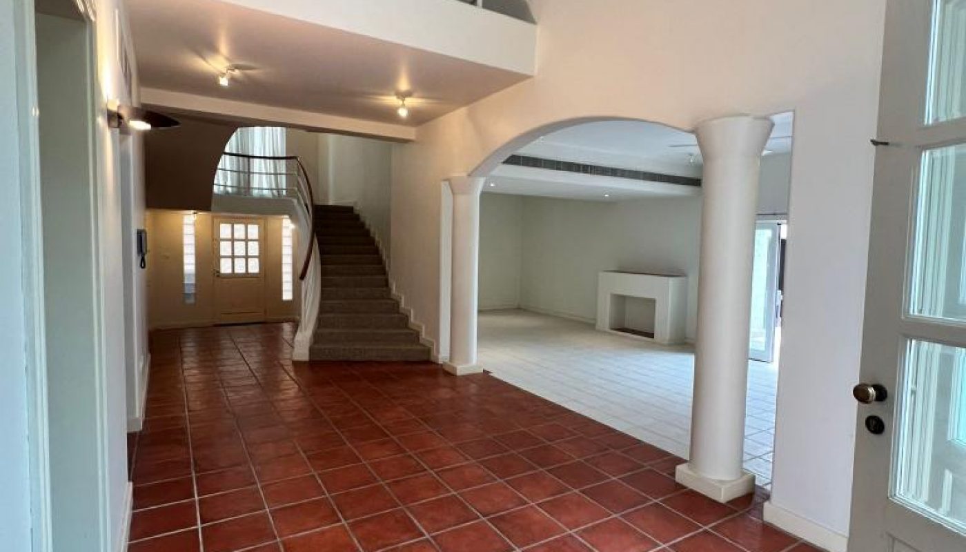 Spacious foyer with terracotta tile floor, staircase leading to an upper level, arched entryway, and view of a living area with a fireplace.