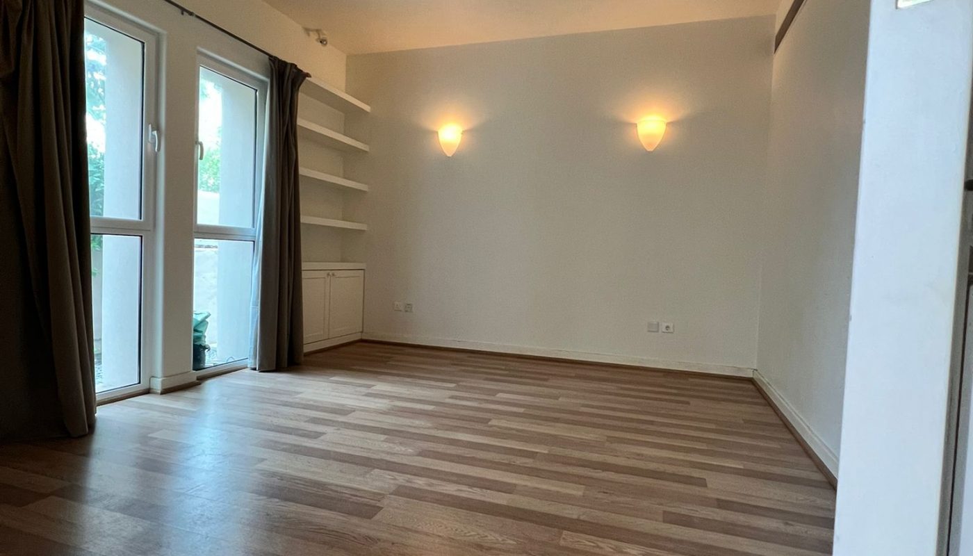 Empty room with wood flooring, two wall lights, a ceiling fan, built-in shelves, and large windows with dark curtains.