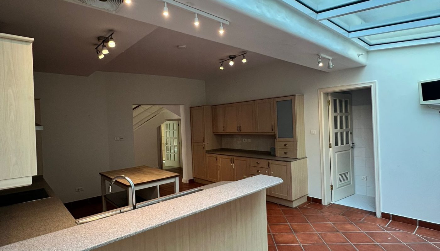 Kitchen with terracotta tile floor, light wood cabinets, and a breakfast bar under a large skylight. Track lighting is installed on the ceiling, and there is a door on the right wall.