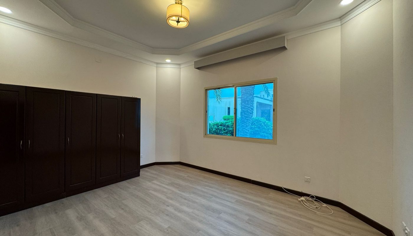 Empty room with wood flooring, dark built-in wardrobes, a window showing greenery outside, light fixture on the ceiling, and some cables on the floor near the wall.