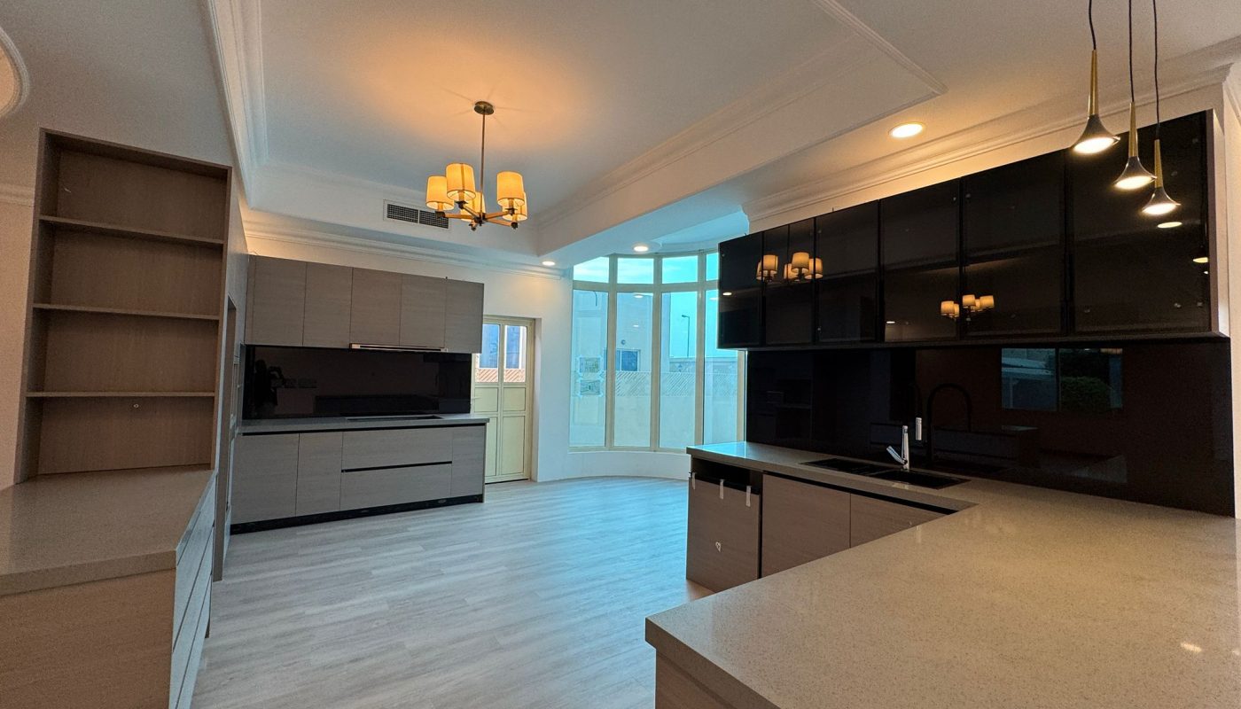 Modern kitchen with light wood cabinets, black upper cabinets, quartz countertops, pendant lights, chandeliers, and large windows letting in natural light.