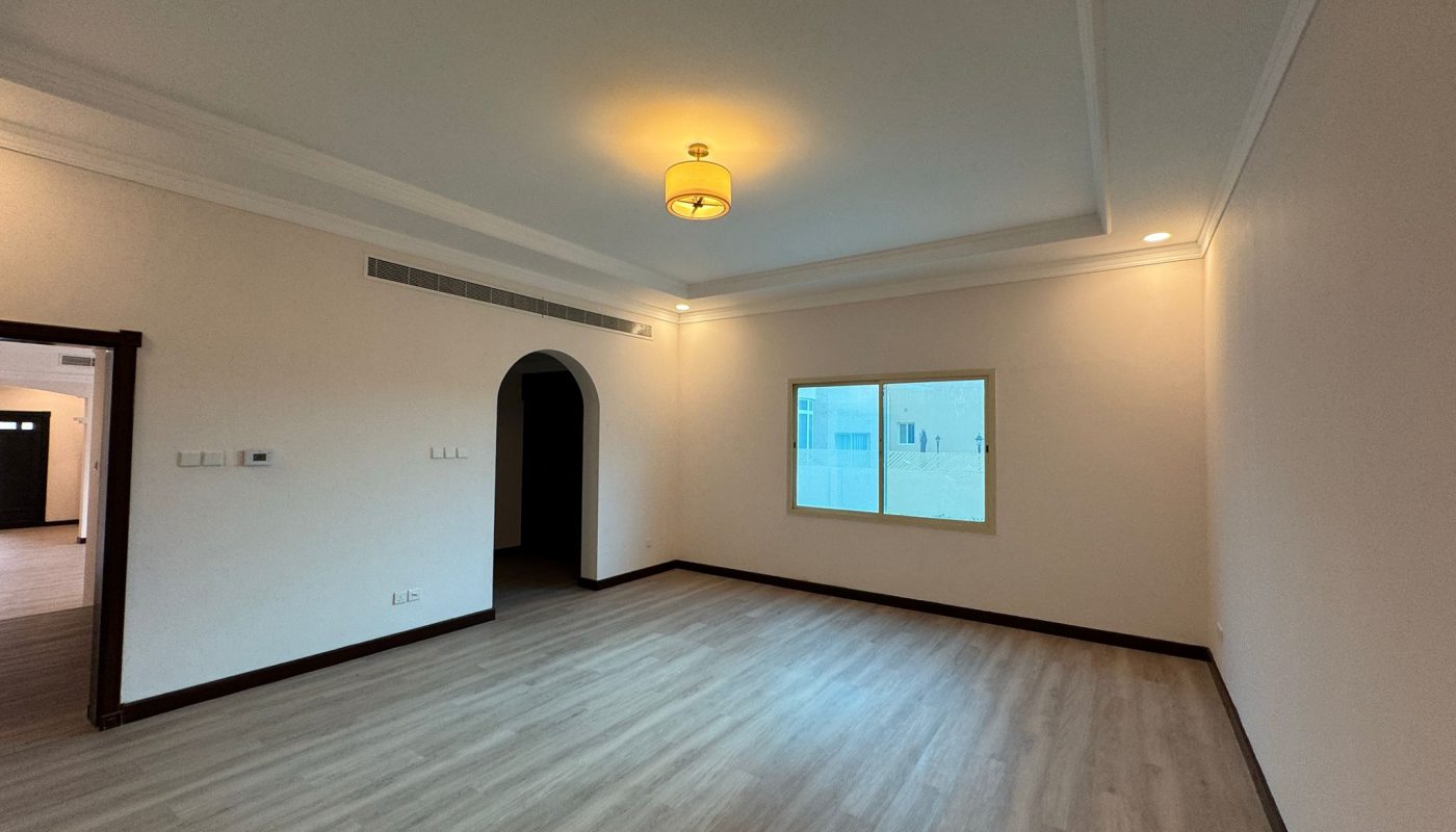 Unfurnished room with light wood flooring, cream-colored walls, a ceiling light, and a window showing a building exterior. An open doorway leads to an adjacent room.