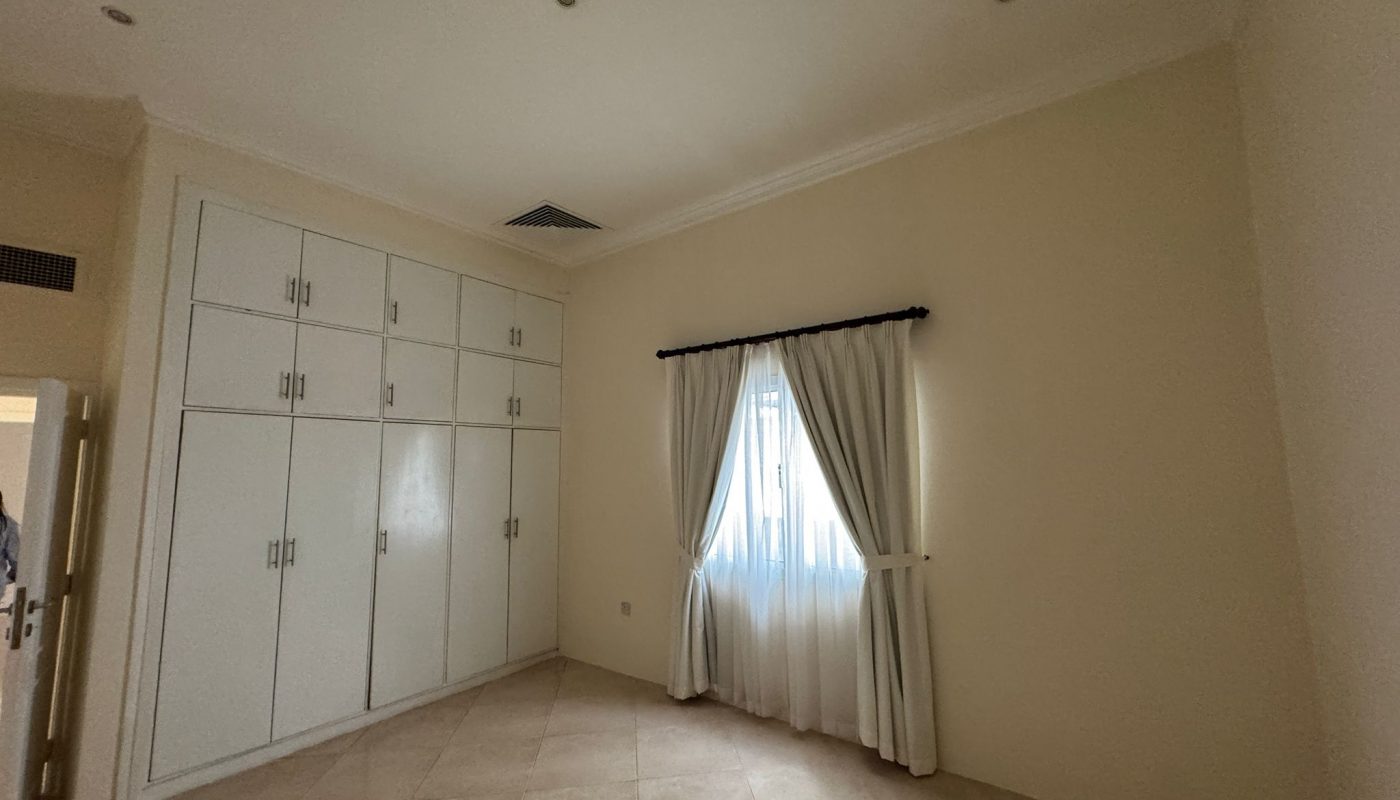 A simple, empty room with tiled floor, cream-colored walls, built-in white cabinets, and a window covered by white curtains.