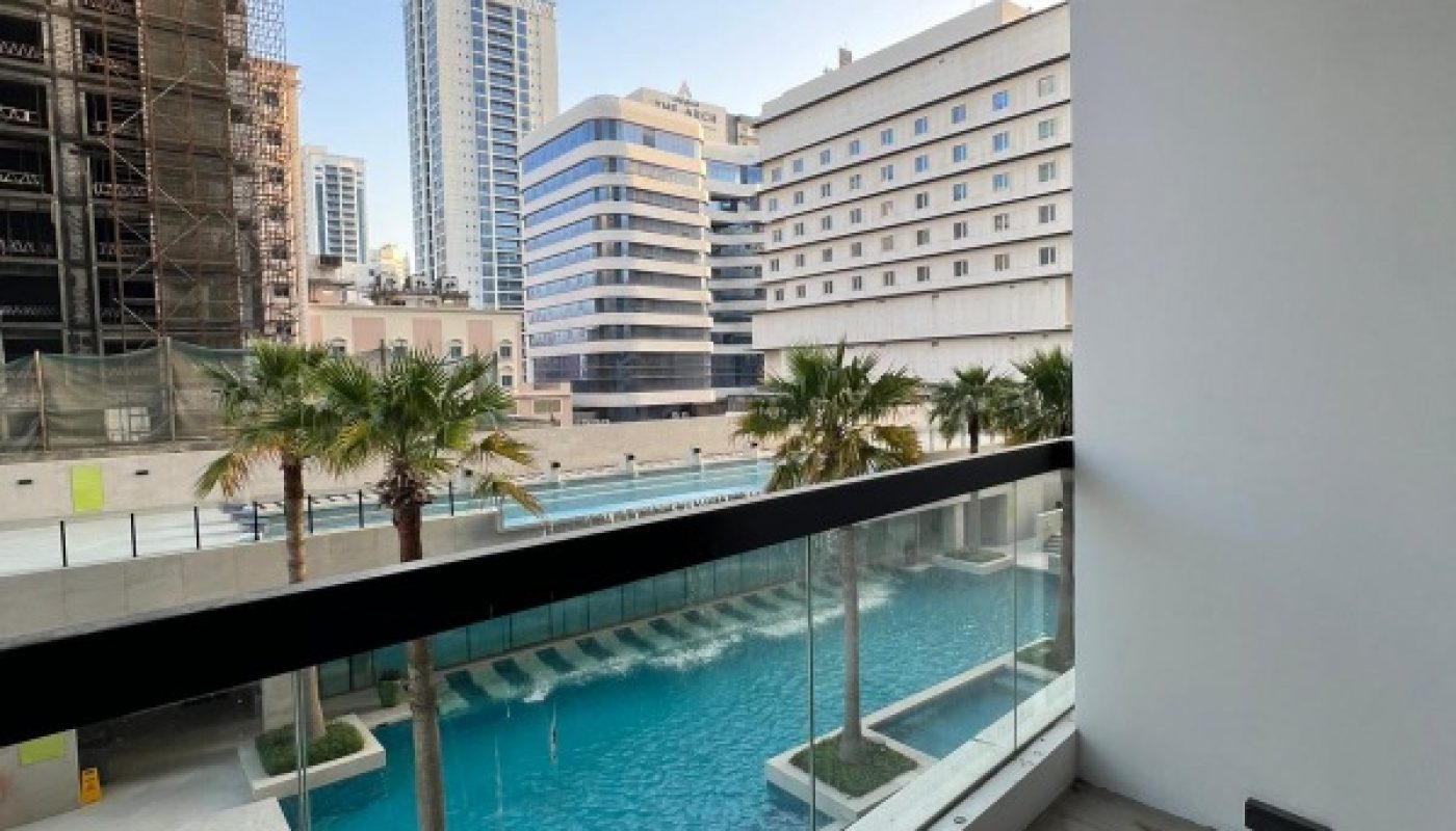 View from a balcony overlooking a pool with palm trees, surrounded by modern high-rise buildings and a construction site on the left.