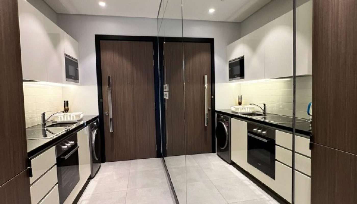Modern galley kitchen with wood and white cabinets, built-in appliances, tile floor, and a large mirrored wall reflecting the space.