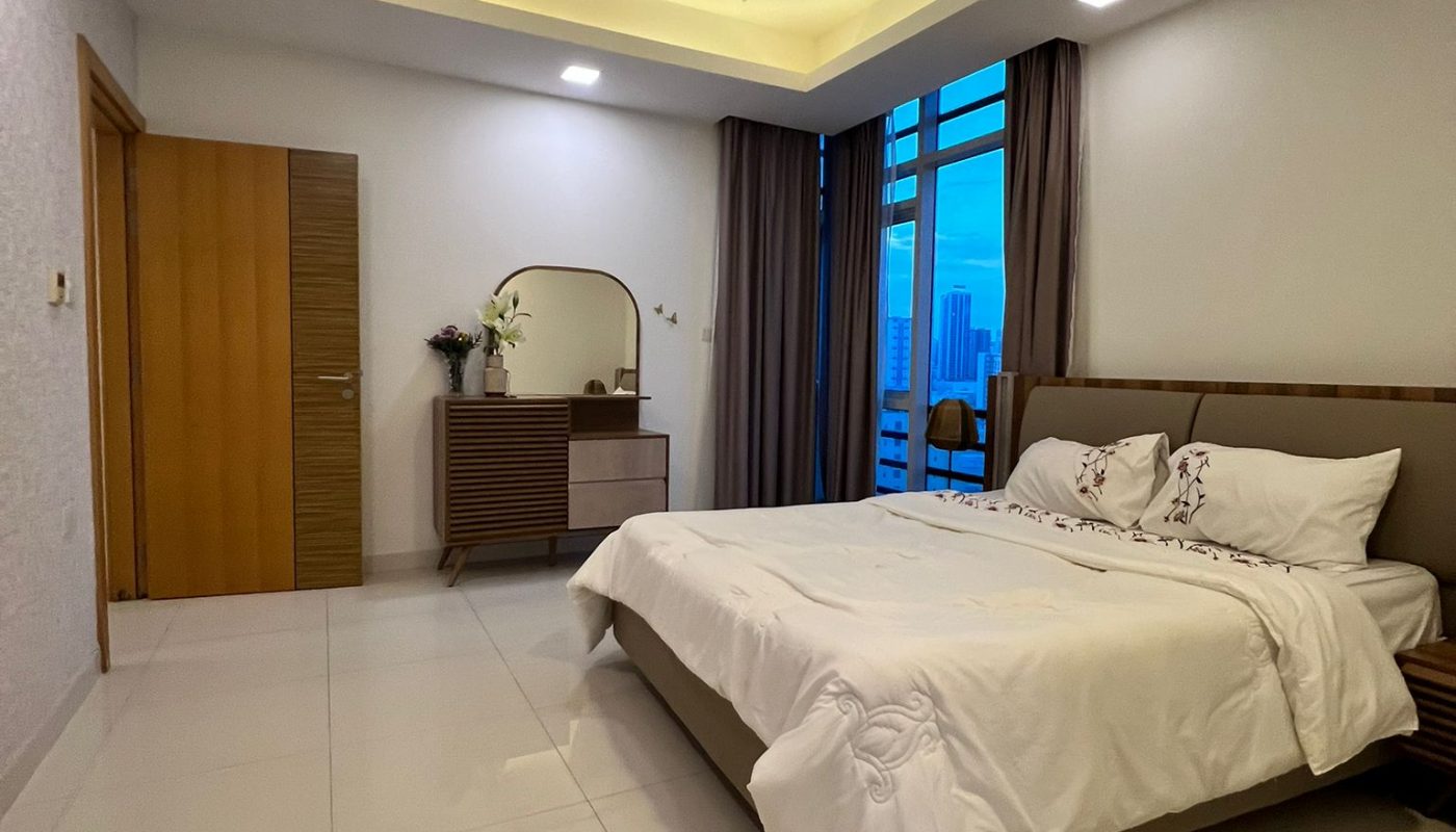 Modern bedroom with a large bed, nightstands, dresser with a mirror, white tiled floor, and floor-to-ceiling windows with closed curtains showing a city view.