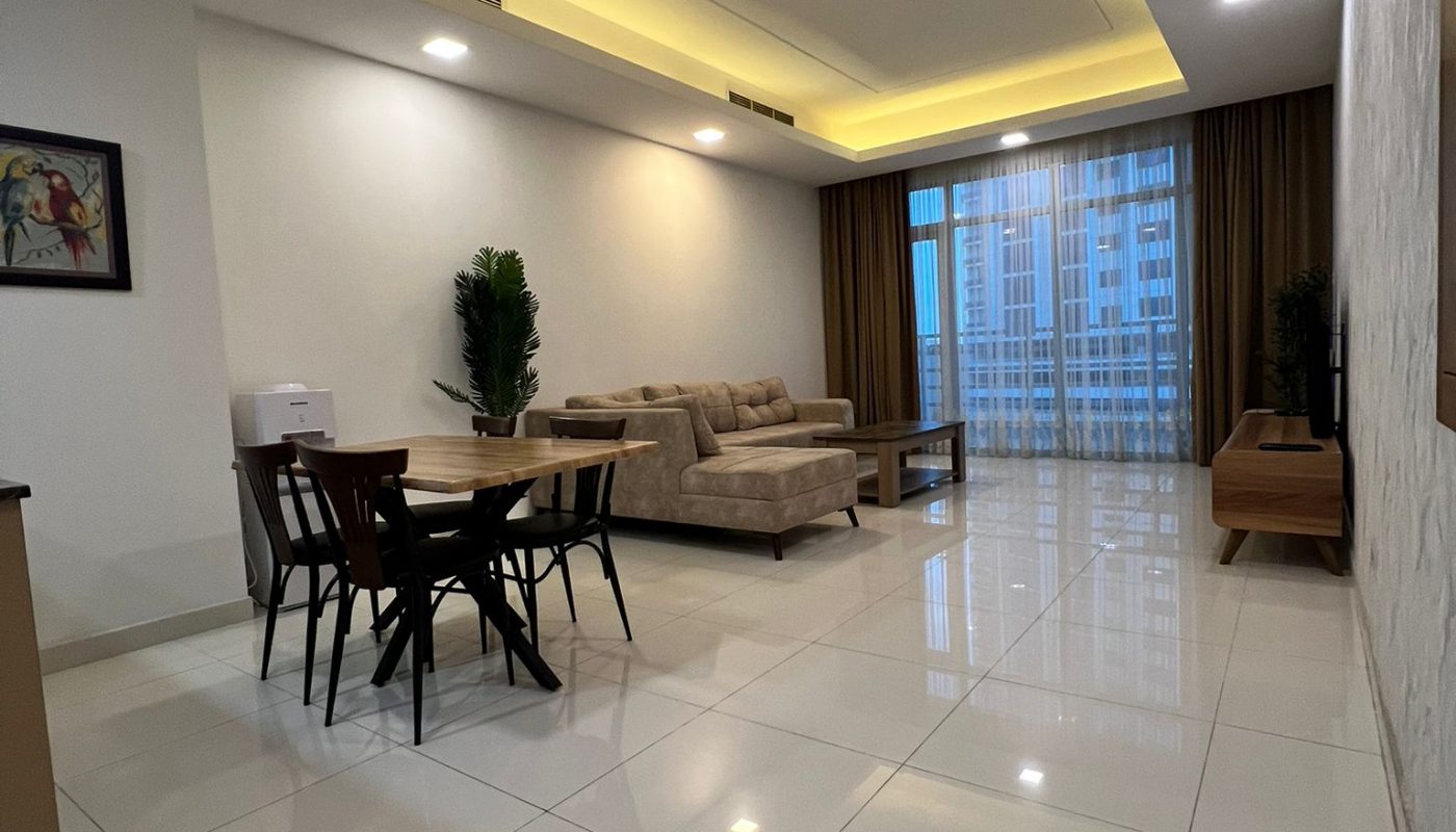 Modern living and dining area with beige sofa, dining table and chairs, wall art, indoor plant, TV unit, large window with curtains, and tiled floor.
