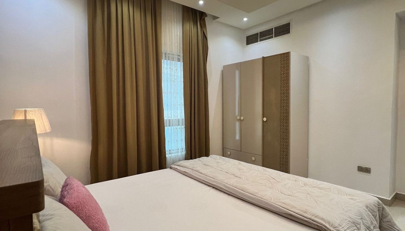 A modern bedroom with a double bed, brown curtains, a wardrobe, and a ceiling with recessed lighting.
