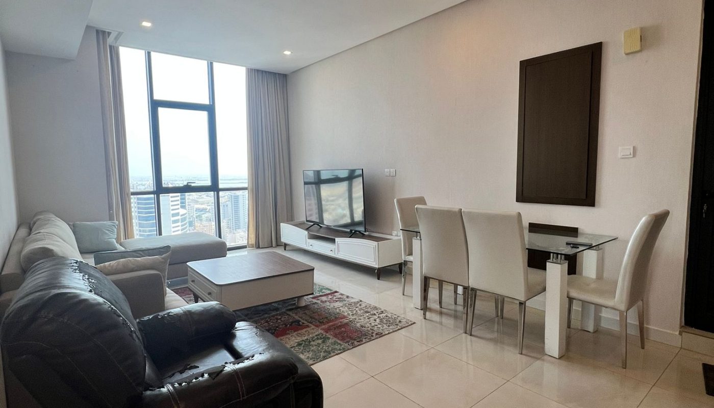 Modern living and dining area with tiled floors, a sectional sofa, armchair, coffee table, TV on a stand, dining table with six chairs, and large window with city view.