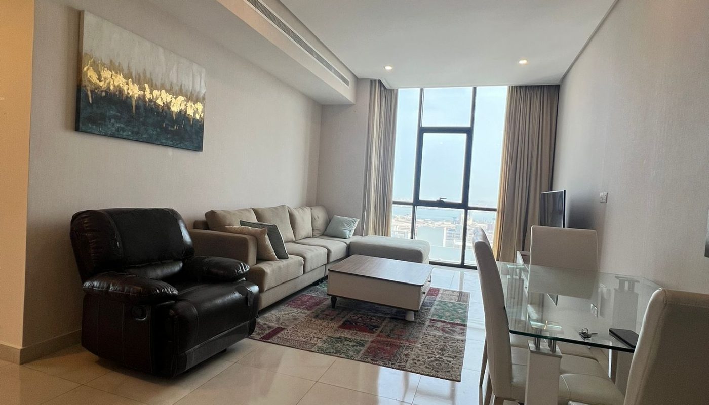Modern living room with a black recliner, beige couch, coffee table, dining table with four chairs, large window, and wall art above the sofa.