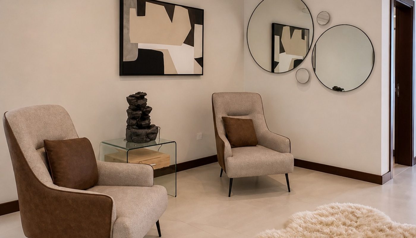 A modern living room with two armchairs, a glass side table, abstract wall art, round mirrors, and a fluffy beige rug on a tile floor.