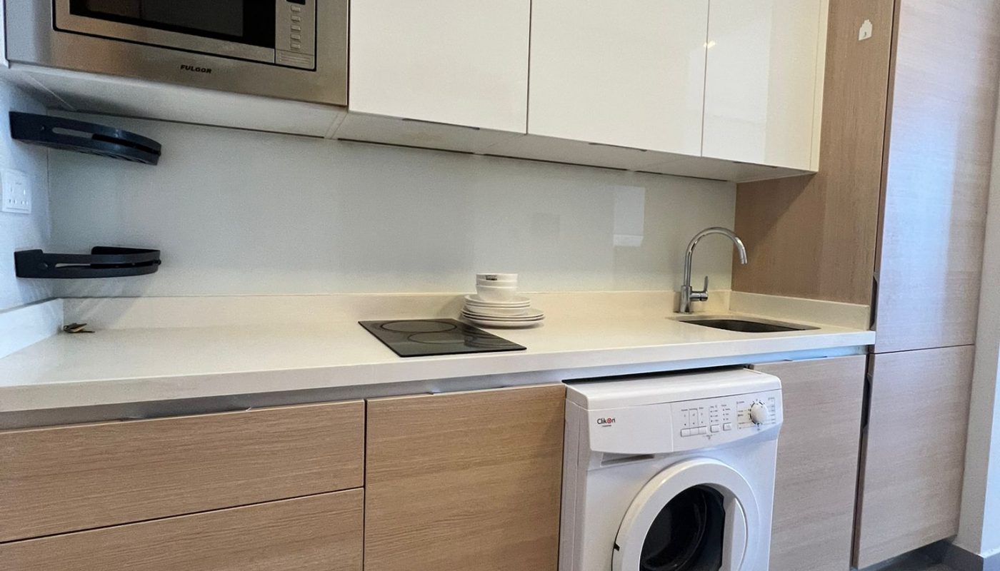 Modern kitchen with light wood and white cabinets, built-in microwave, sink, electric cooktop, and a front-loading washing machine under the counter.