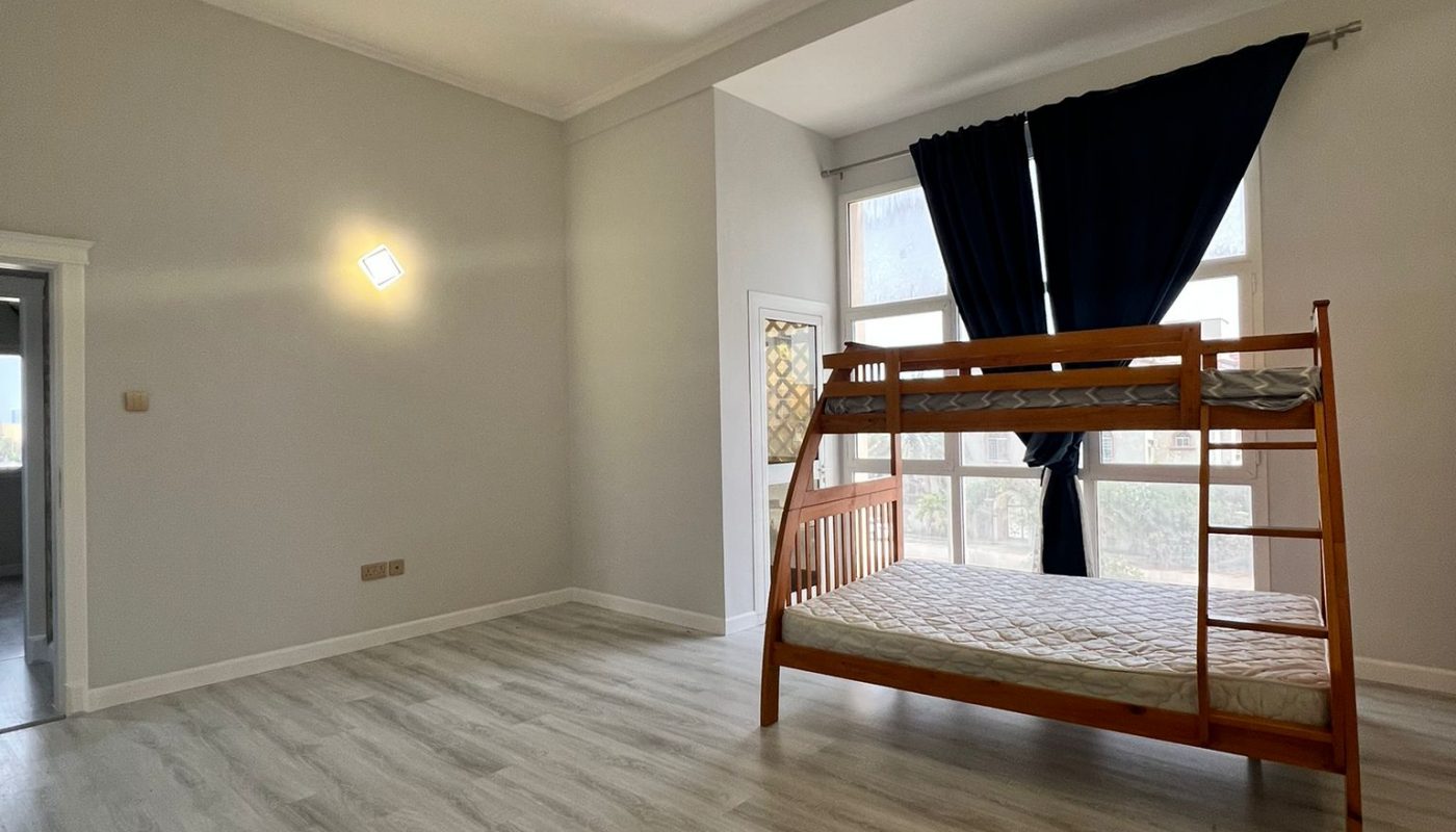 A spacious, unfurnished room with light wood flooring, a wooden bunk bed near large windows with dark curtains, and white walls.