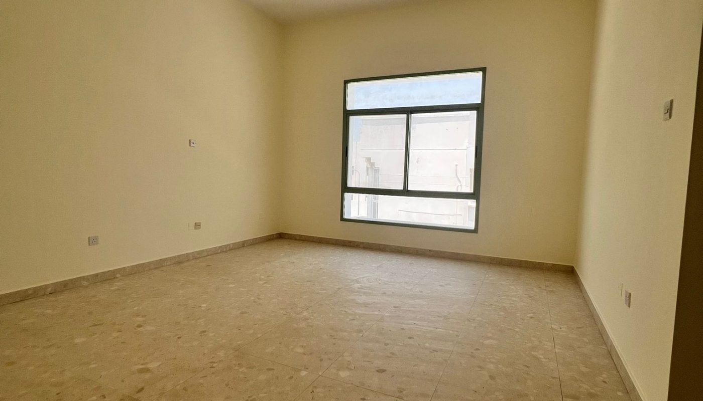 Empty room with beige walls and tiled floor, a large window on one wall, and a modern ceiling light fixture.