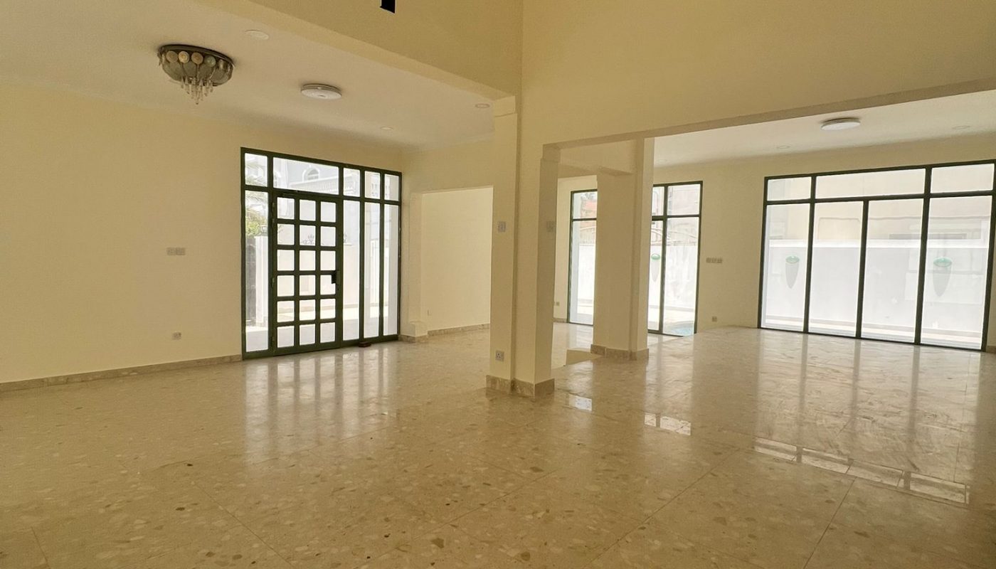 Spacious empty room with tiled floor, beige walls, large windows, glass doors, and two ceiling light fixtures.