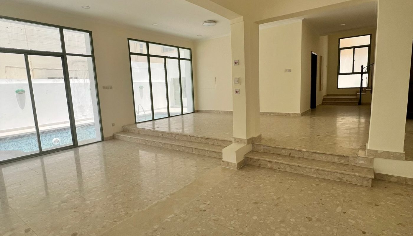 Spacious, empty living area with tiled floor, large sliding glass doors leading to a pool, and steps connecting two levels.