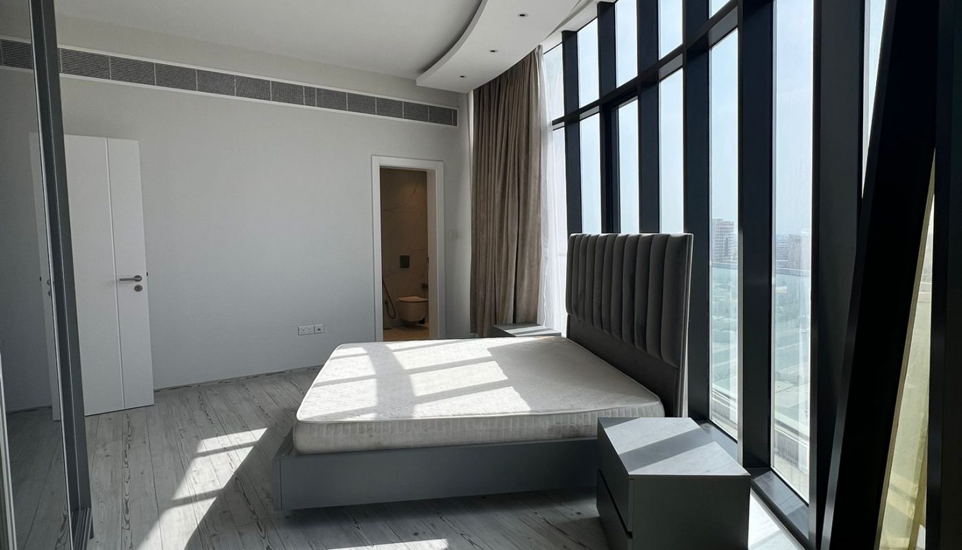 A modern, minimalistic bedroom with a large bed, nightstand, and floor-to-ceiling curved windows letting in natural light.