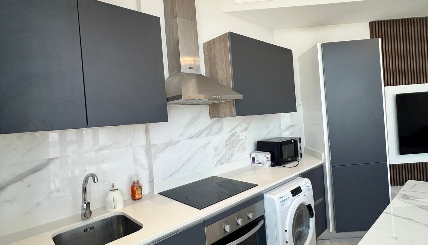 Modern kitchen with dark cabinets, a sink, electric stove, washing machine, microwave, and marble countertops and backsplash.
