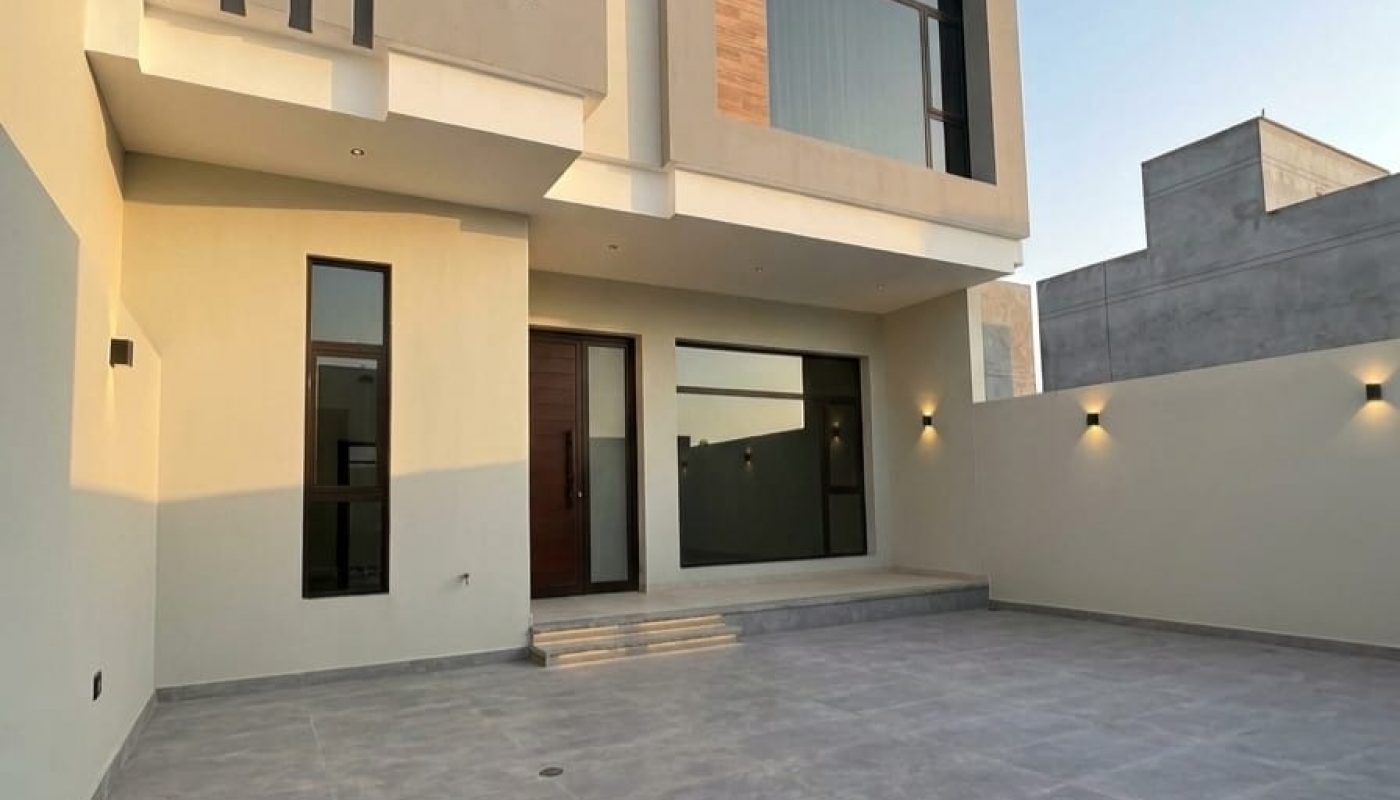 Modern two-story house with large windows, wood and gray accent panels, a flat roof, and a spacious tiled front courtyard.