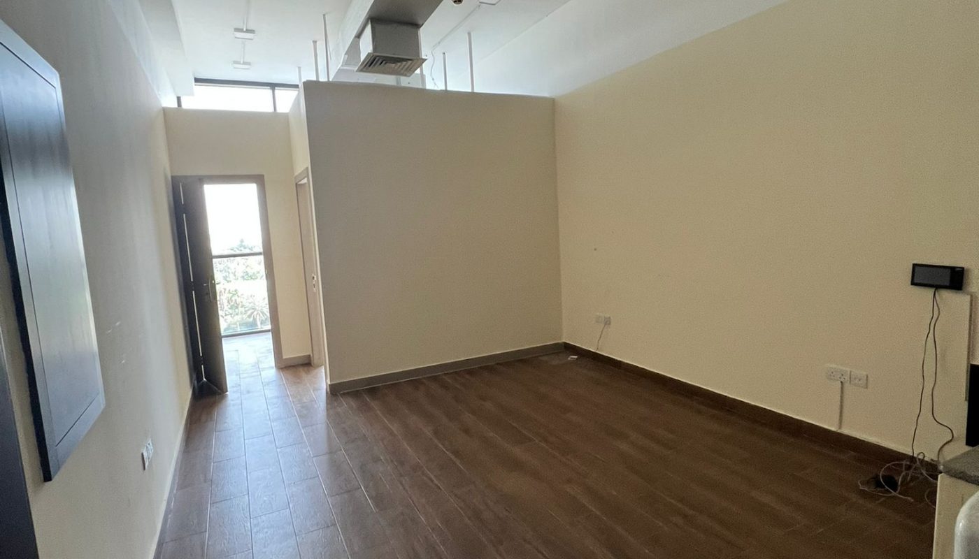 Empty room with wood-look tile flooring, beige walls, ceiling vents, and a windowed door letting in natural light at the far end.