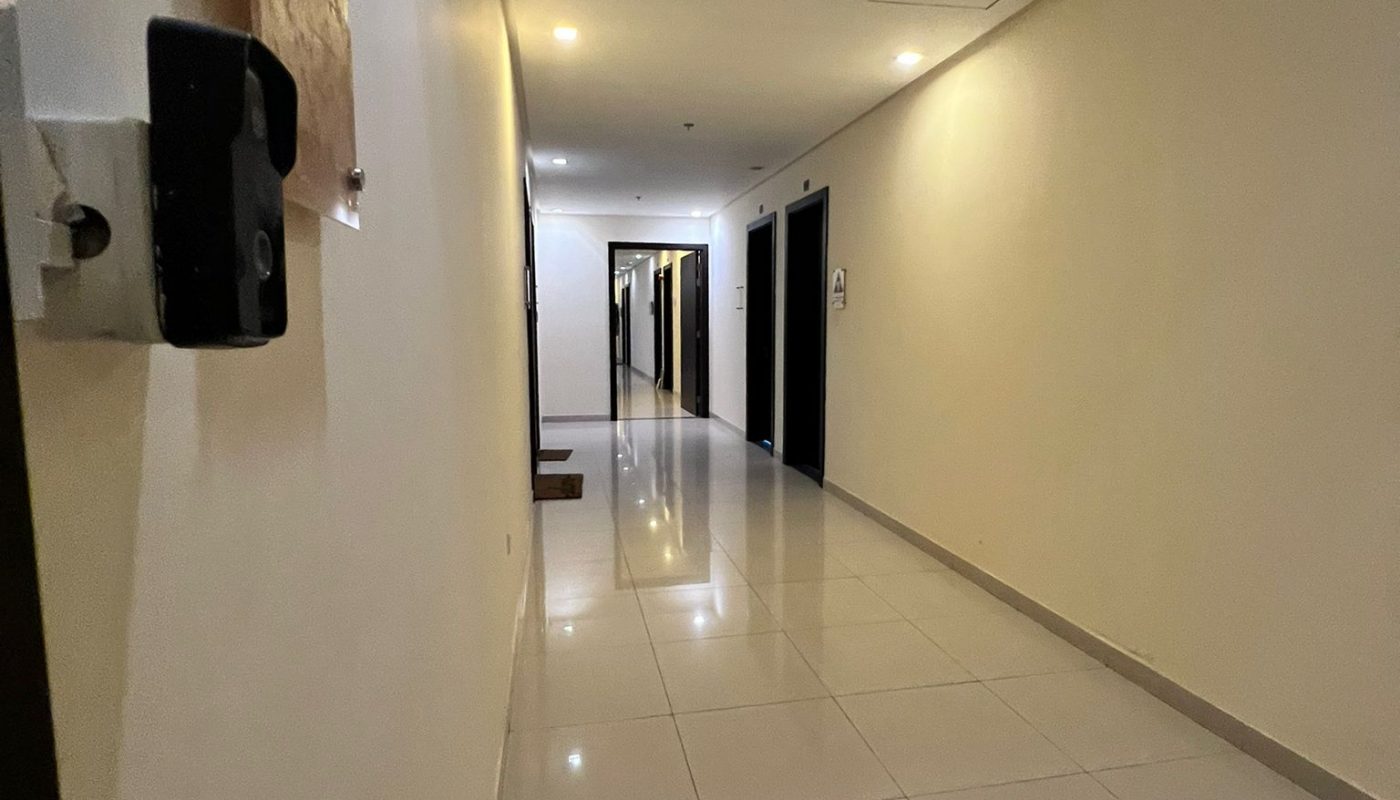 A clean, brightly lit hallway with tiled floors, cream-colored walls, and several doors along the corridor.