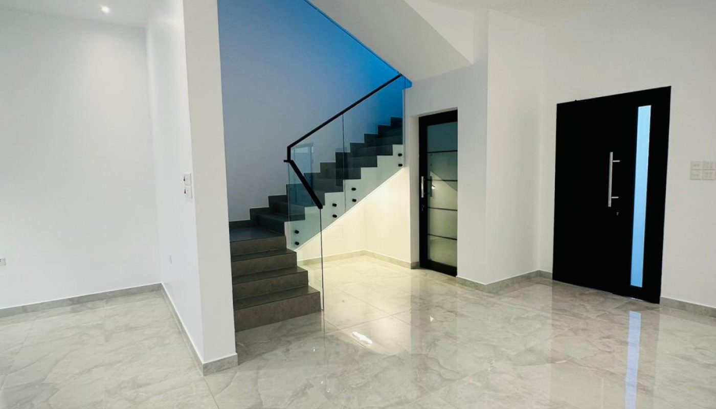 Modern foyer with a glass-railed staircase, black door, and tiled floor.