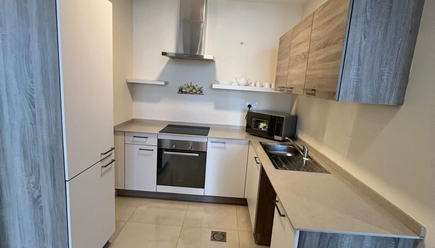 Modern kitchen with light wood cabinets, built-in appliances, a stainless steel oven and range hood, and a beige tile floor. Countertops are clear, with minimal decor and dishware.