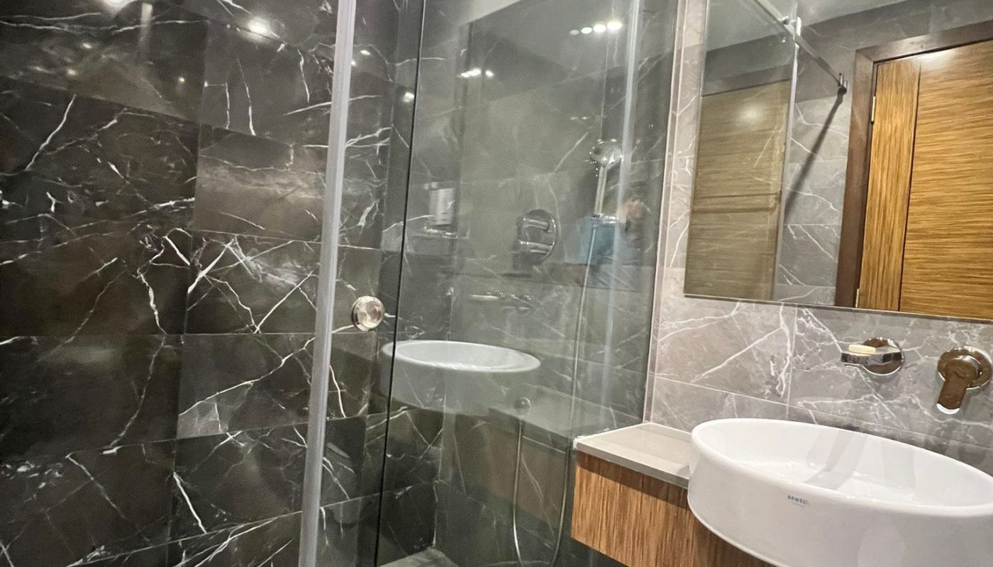 Modern bathroom with a glass shower enclosure, marble-patterned walls and floor, a wall-mounted sink, and a large mirror.