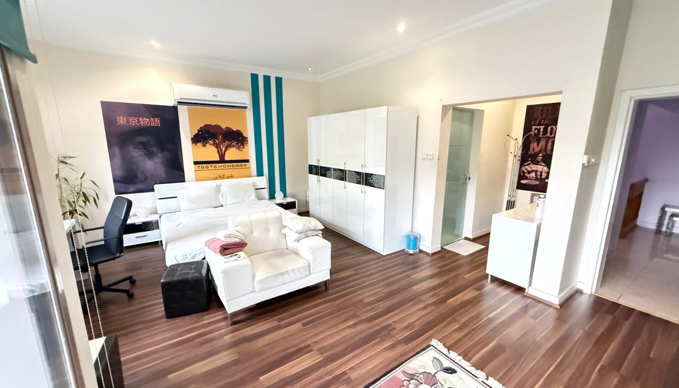Bright modern room with white furniture, a rug, painted wall stripes, large posters, a workspace, and visible entry to a bathroom and adjacent room.
