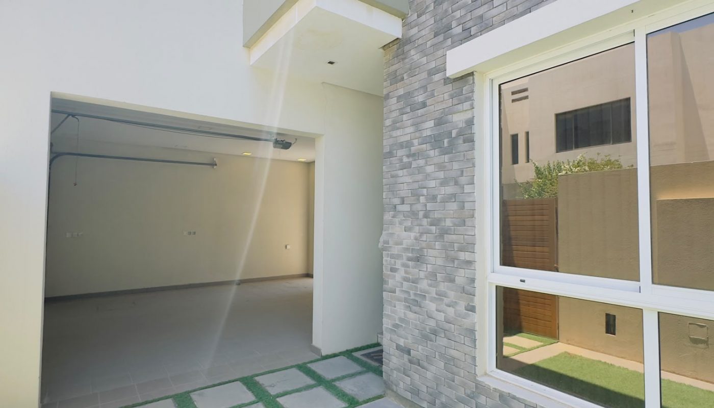 A modern house exterior with gray brick walls, large windows, a garage, and an artificial grass lawn under bright daylight.