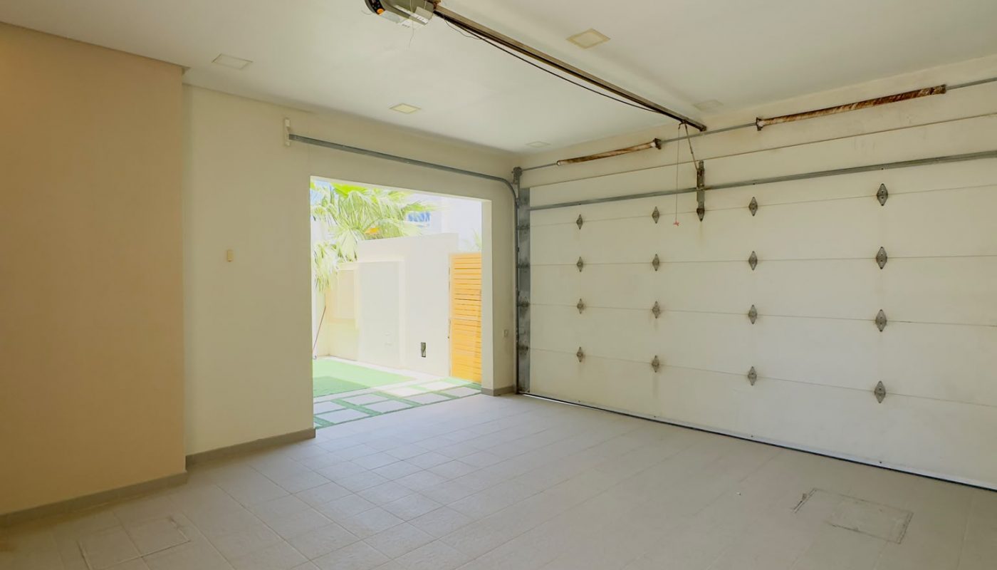 Empty two-car garage with tiled floor, closed white sectional garage door, and open side door letting in natural light.