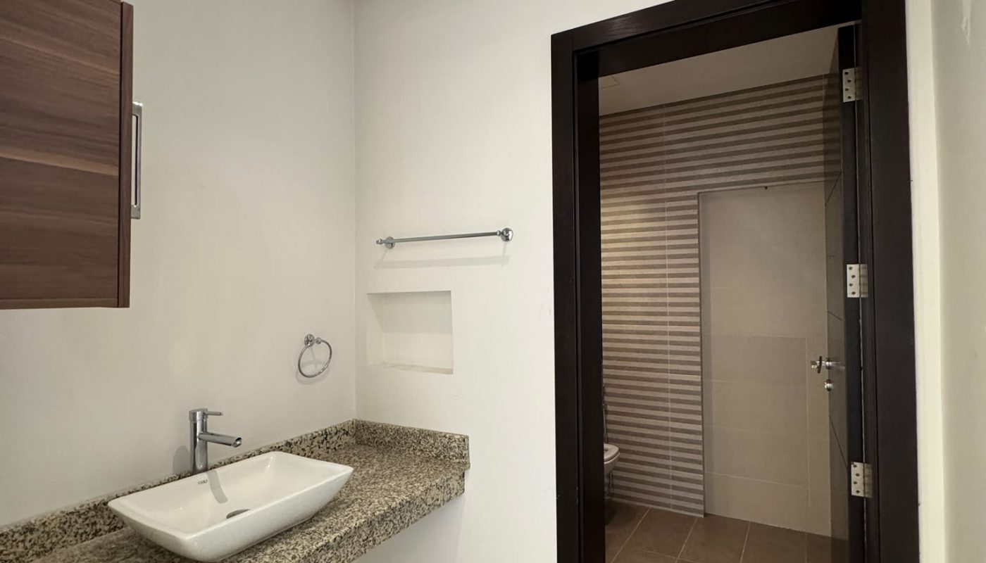 Modern bathroom with granite countertop, rectangular vessel sink, wall-mounted cabinet, towel rack, and a doorway leading to a tiled shower area.