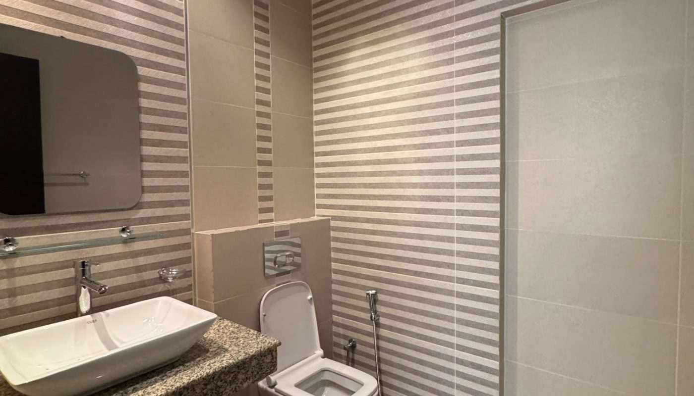 Modern bathroom with striped beige walls, a wall-mounted toilet, a rectangular sink on a granite countertop, a mirror, and a handheld bidet spray.