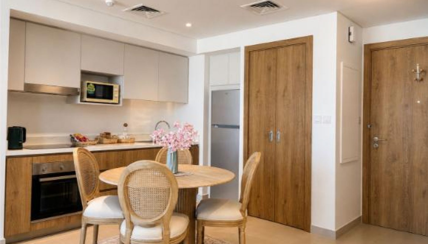 Modern kitchen and dining area with wooden cabinets, a round table with four chairs, and a vase of pink flowers on the table.