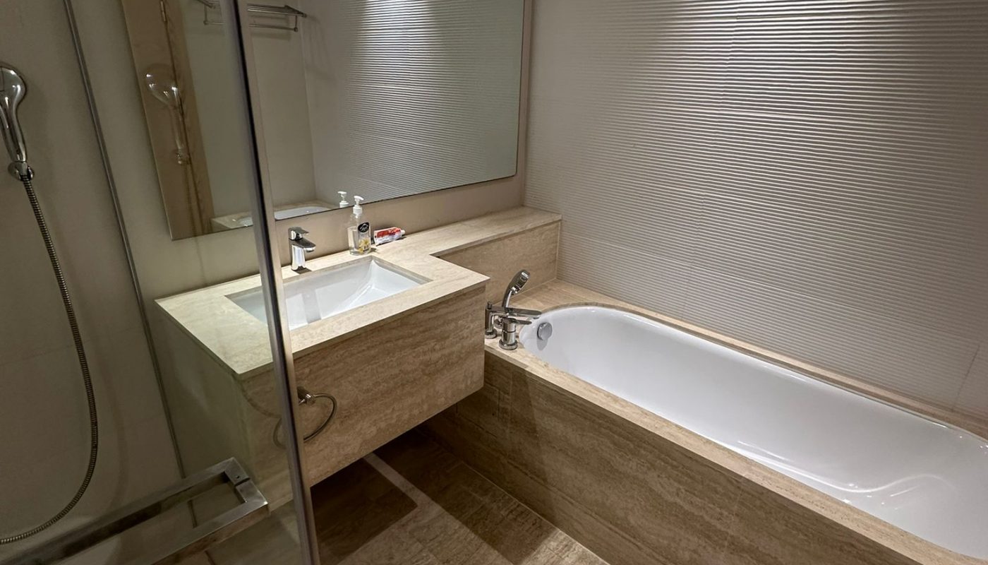 Modern bathroom with a walk-in shower, built-in bathtub, large mirror above a sink, and beige tile flooring and walls.