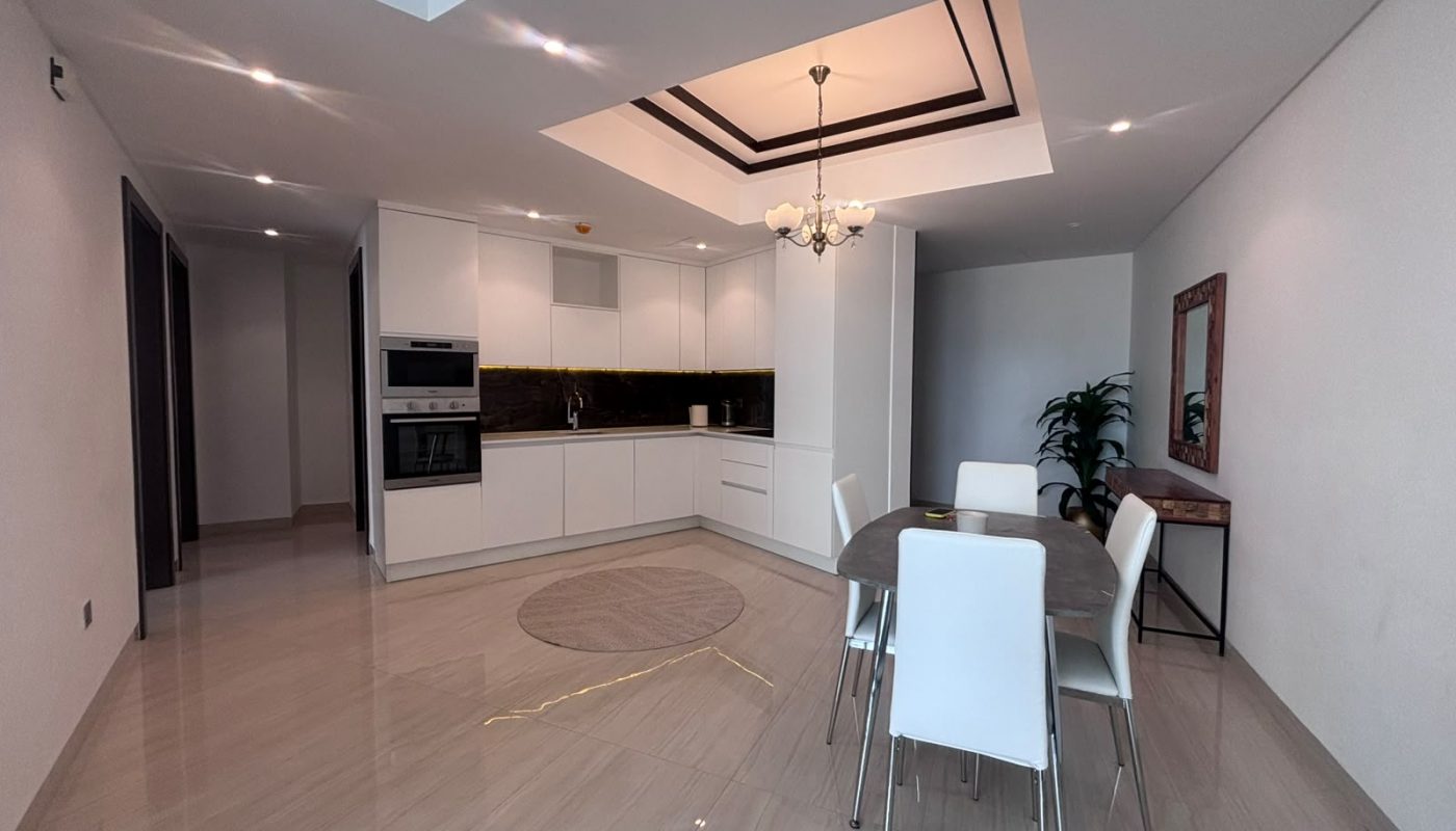 Modern kitchen and dining area with white cabinets, built-in appliances, a dining table with six chairs, and a decorative mirror on the wall.
