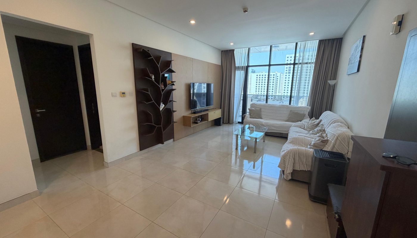 Modern living room with tiled floor, two white sofas, a glass coffee table, TV on a stand, decorative shelving, and large window showing city buildings in the background.