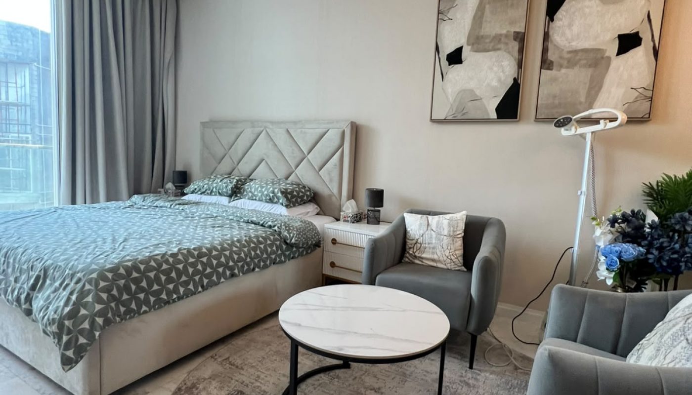 Modern bedroom with a double bed, two armchairs, a round coffee table, abstract wall art, and large window with curtains. Neutral color palette and contemporary decor.