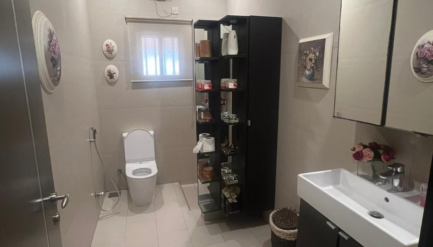 Modern bathroom with a toilet, sink, black storage cabinets, decorative wall plates, and bright overhead lighting.
