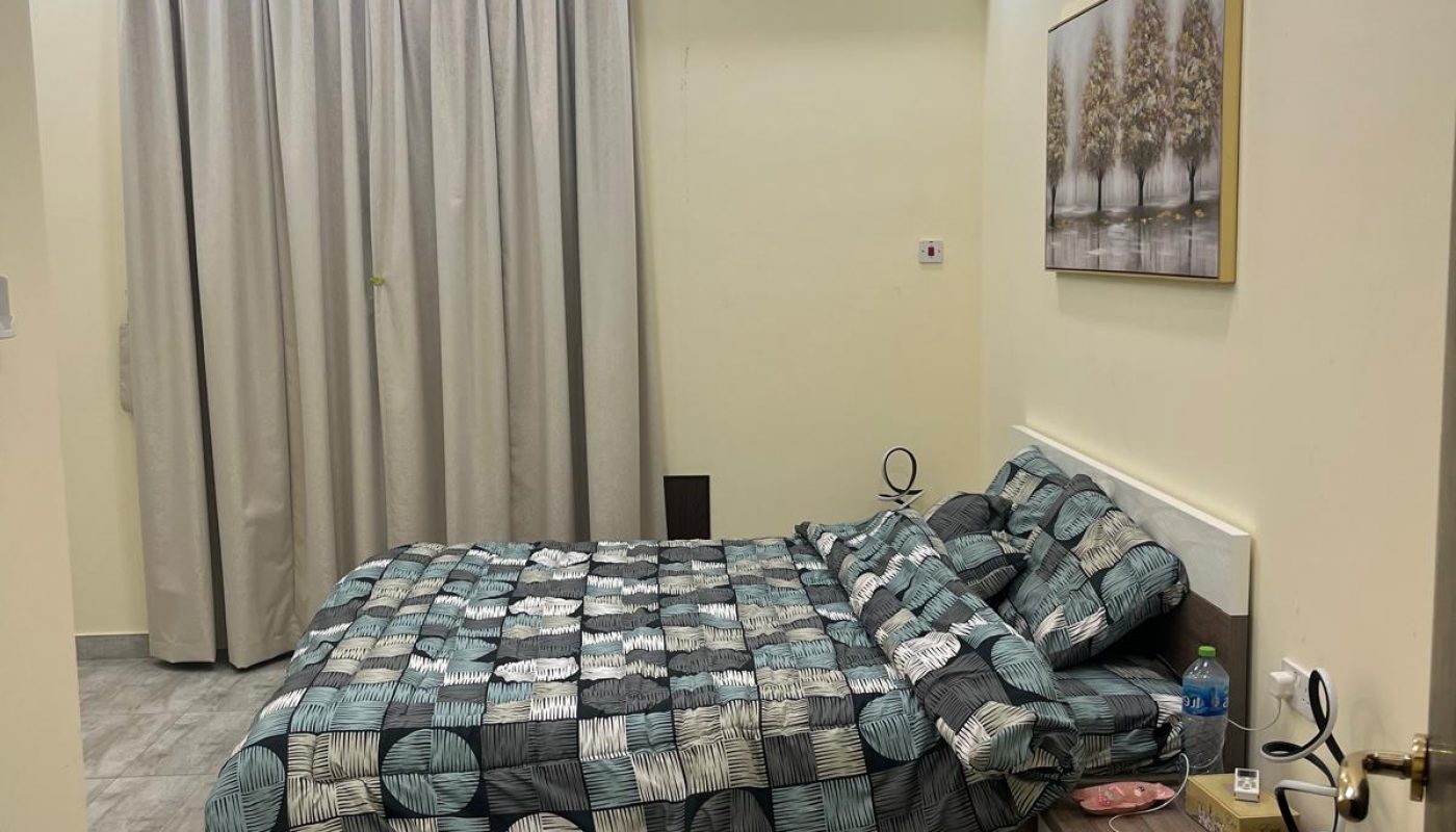 A modern bedroom with a neatly made bed, nightstand, abstract bedding, wall-mounted air conditioner, curtain, artwork, and contemporary ceiling light.