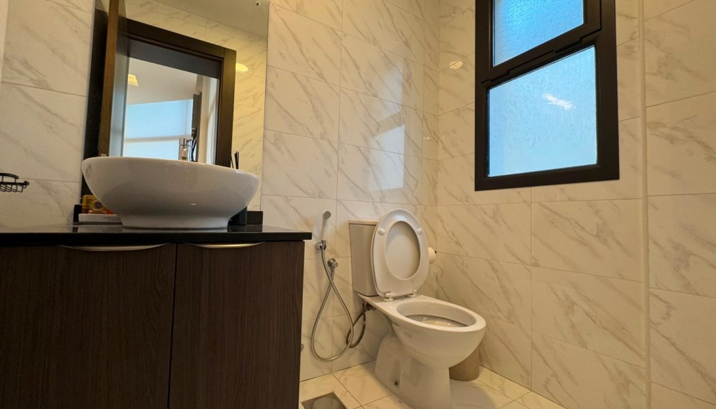 Modern bathroom with marble tiles, a vessel sink on a dark wooden vanity, a wall mirror, a toilet with the lid up, a bidet spray, and a frosted window.