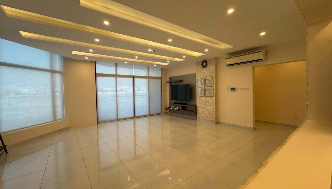 Spacious modern living room with tiled floors, recessed ceiling lights, large windows, a wall-mounted TV, and an air conditioner above.