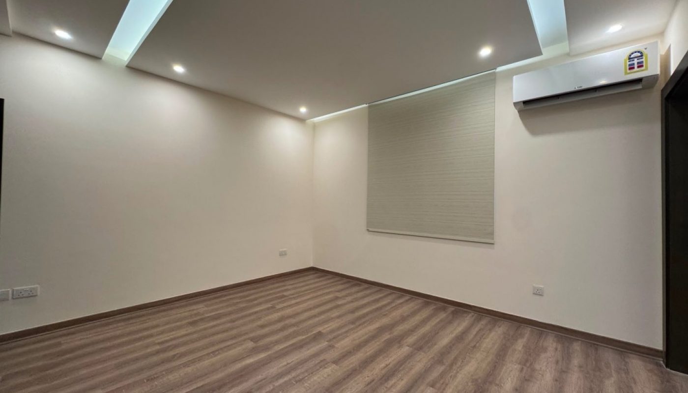 Empty room with wooden flooring, white walls, recessed ceiling lights, a window with a closed blind, and an air conditioning unit on the wall.