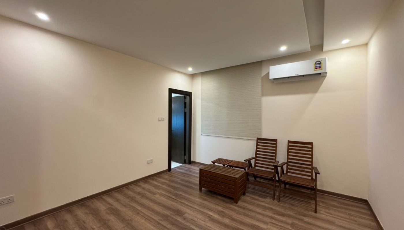 Minimalist room with two wooden chairs, a small table, wood flooring, beige walls, ceiling lights, window blinds, and a wall-mounted air conditioner.
